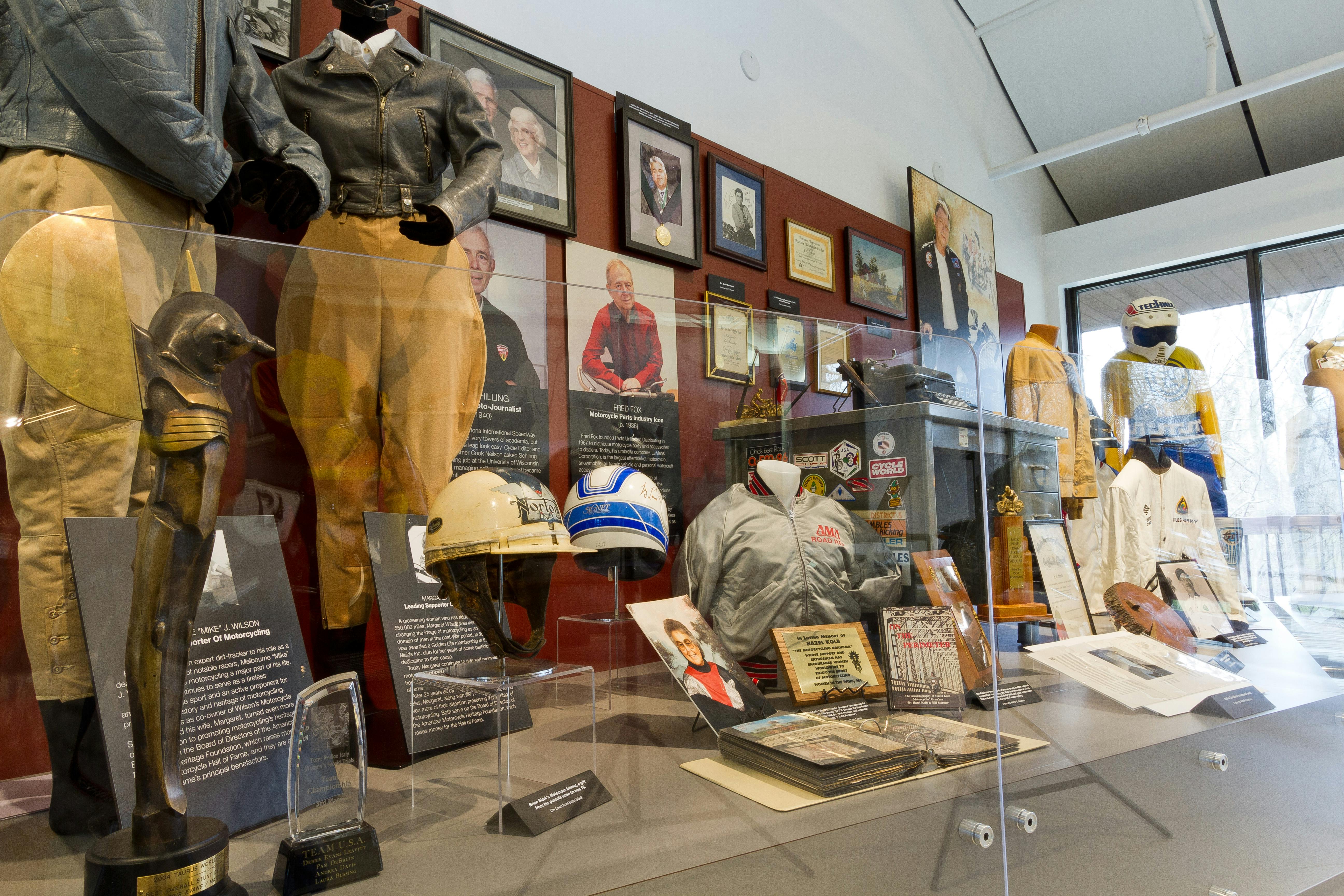 博物馆展览展示航空纪念品，包括夹克、头盔、牌匾、照片和信息牌匾。