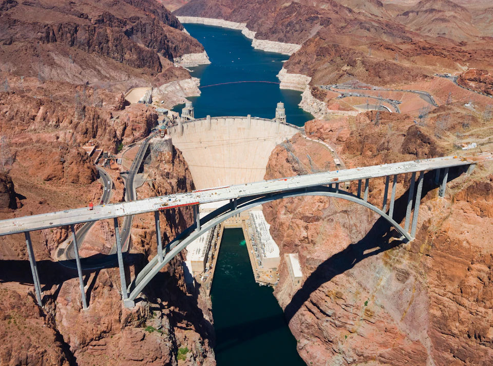 Aerial view of the Hoover Dam with a bridge spanning across the canyon and water reservoir in the background.