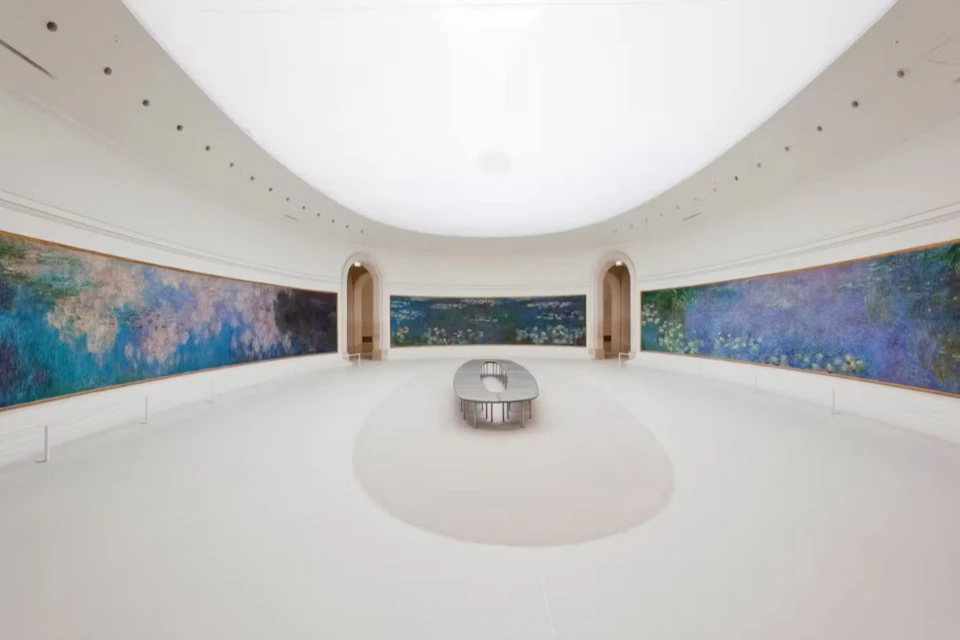 A spacious gallery room with curved walls displaying large impressionist paintings, featuring a central oval bench.