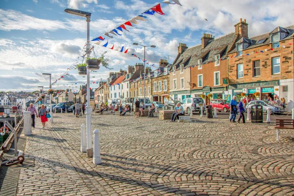 A cobblestone street lined with colorful buildings, cars, and pedestrians, decorated with red, white, and blue bunting.