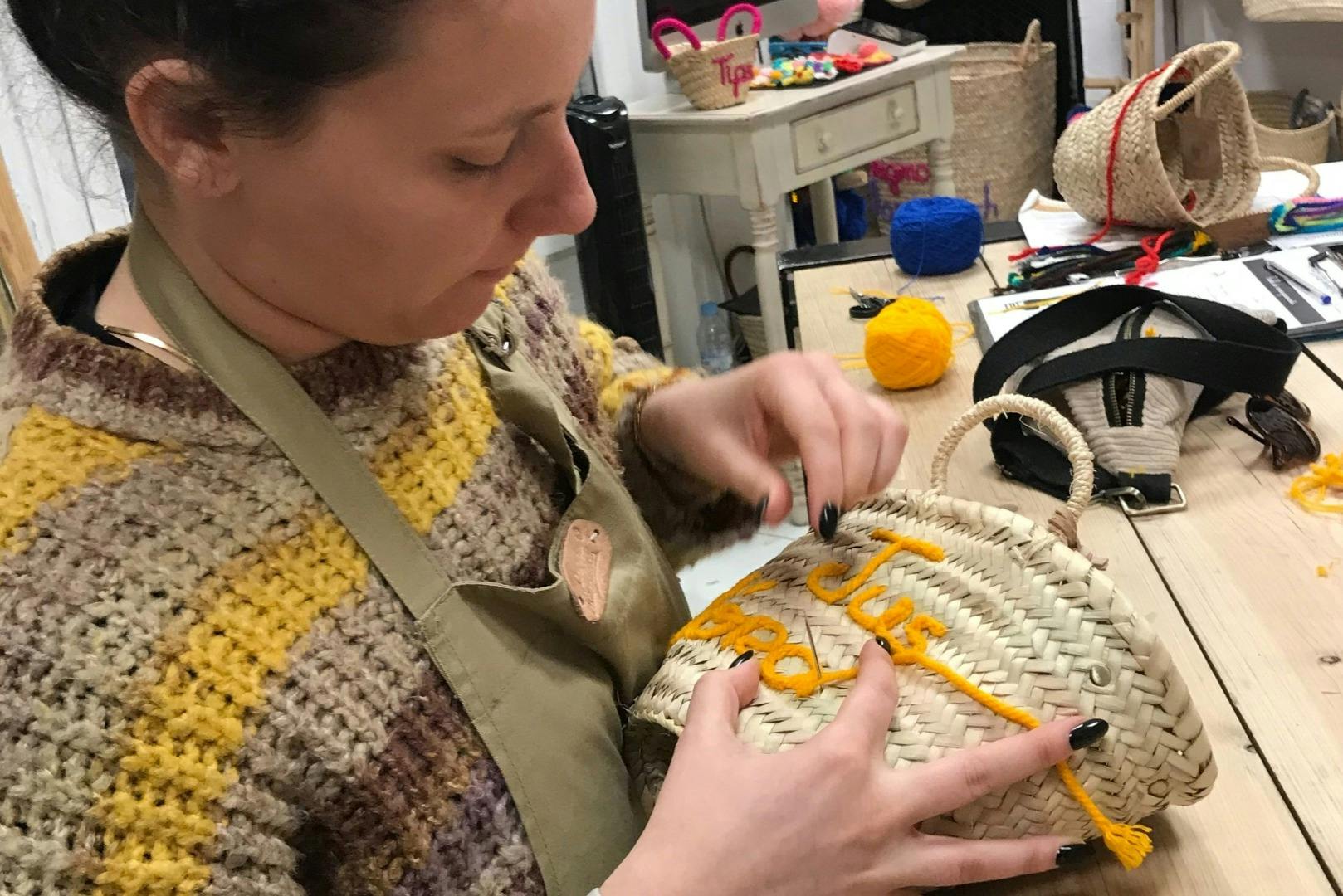 Ένα άτομο που φοράει πλεκτό πουλόβερ και ποδιά διακοσμεί ένα πλεκτό καλάθι με πορτοκαλί γράμματα σε ένα δωμάτιο χειροτεχνίας.