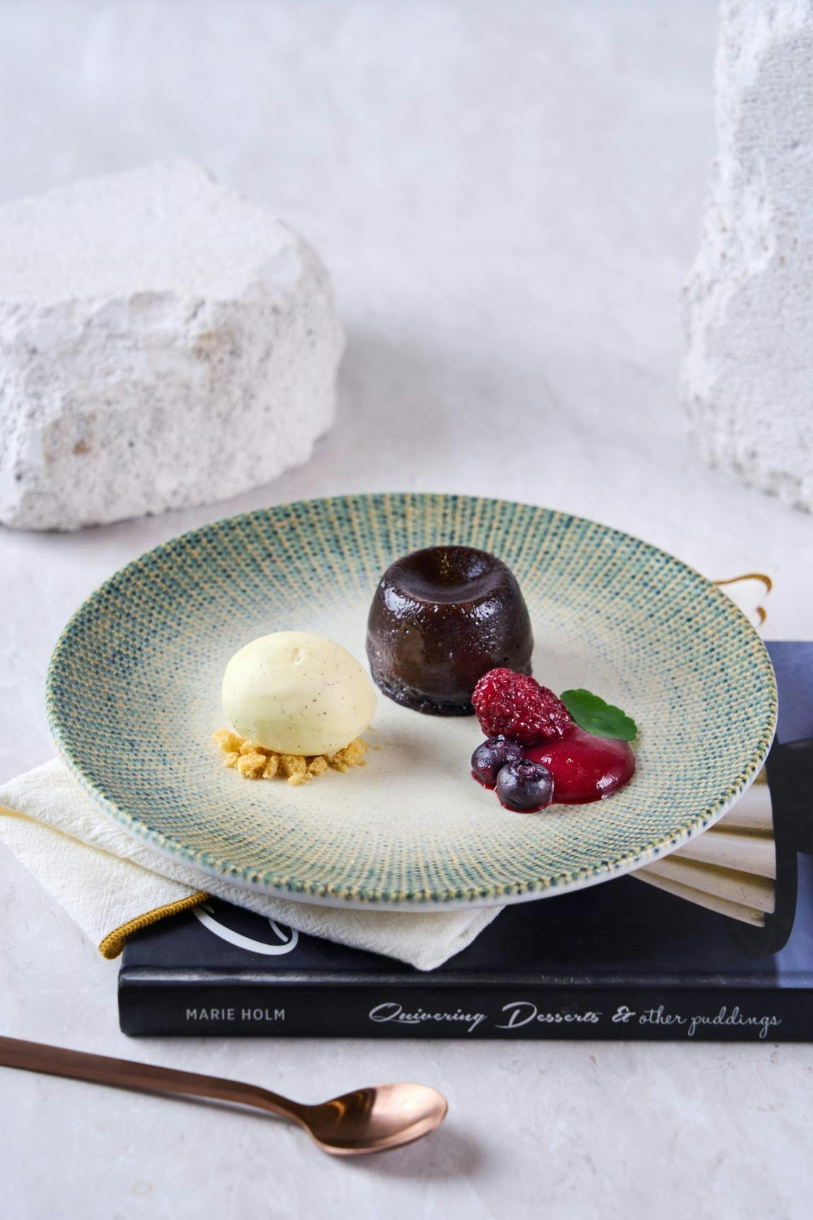A dessert plate with a molten chocolate cake, vanilla ice cream, berries, and sauce, placed on a napkin over a book.