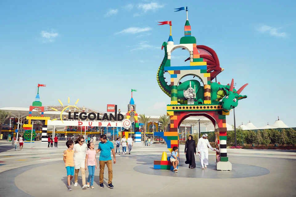 Families walking near a colorful LEGO archway with a dragon, at the entrance of LEGOLAND Dubai under a clear sky.