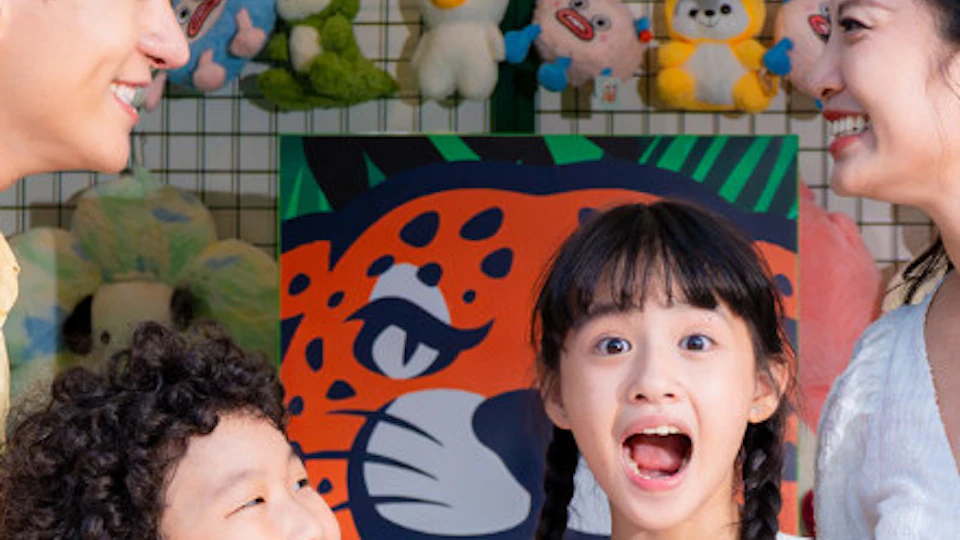 A family with two children holding stuffed toys smiles in front of a carnival game booth decorated with toy prizes.