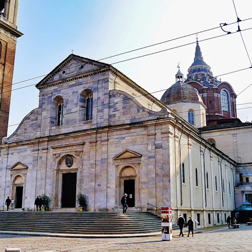 Historisk katedral med ett klocktorn i tegel, stora entrédörrar och människor som går framför. Vajrar och kupolformade konstruktioner är synliga.
