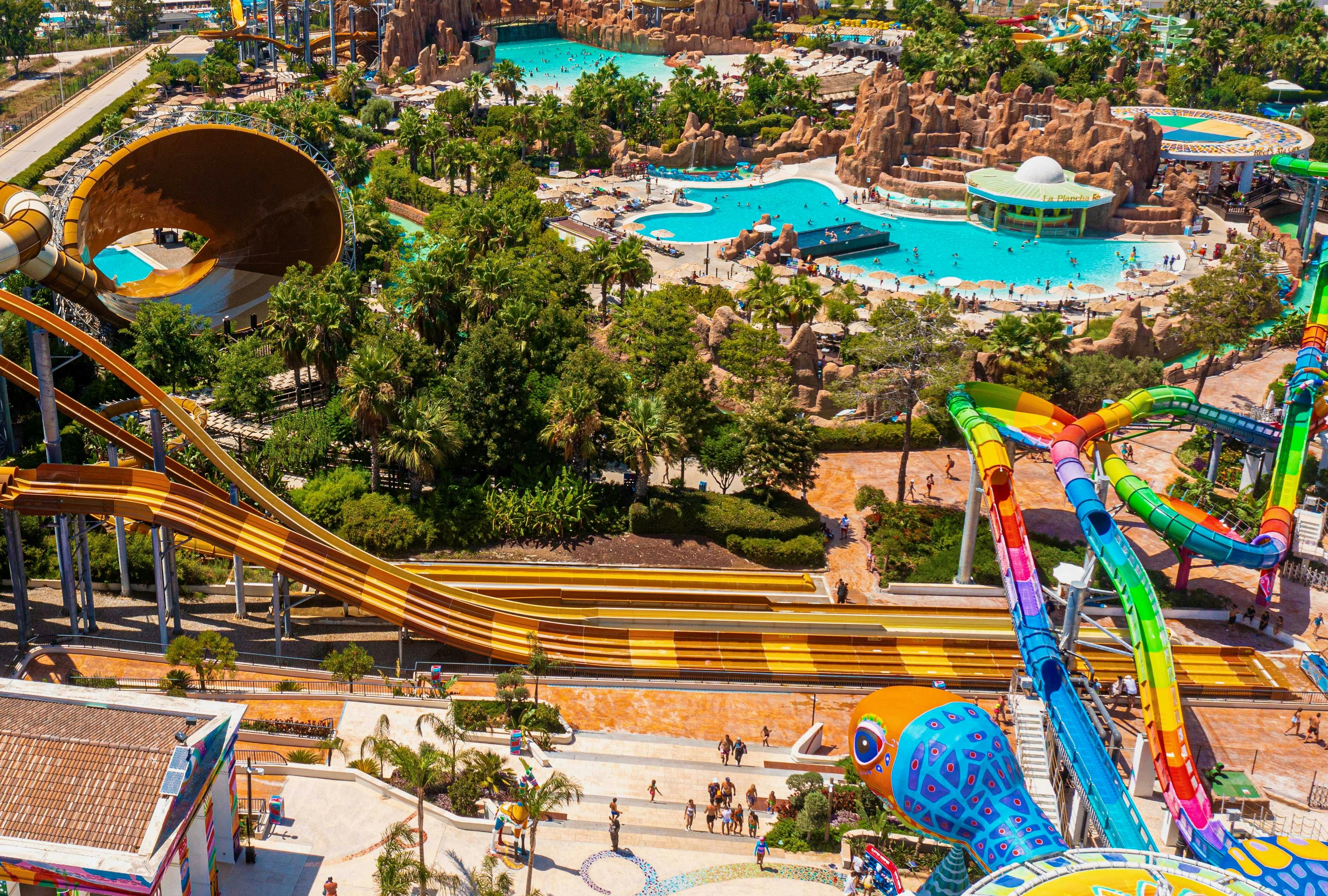 A vibrant water park featuring pools, slides, and lush greenery, with people enjoying the attractions.