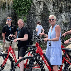 Fyra personer står med röda hyrcyklar nära en klippvägg med vatten som rinner ner.