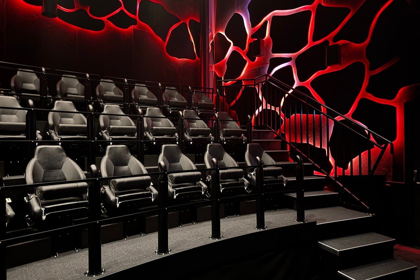 Salle de cinéma vide avec des chaises noires luxueuses et des motifs muraux géométriques rouges et noirs. Places assises surélevées.