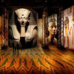 Besökare ser stora statyer och väggmålningar som visar forntida egyptiska faraoner och scener, upplysta i ett utställningsutrymme.