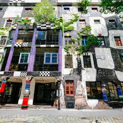 Färgglad, eklektisk byggnadsfasad med rutmönster, livfulla kolumner, varierade fönster och grönska som växer på utsidan.