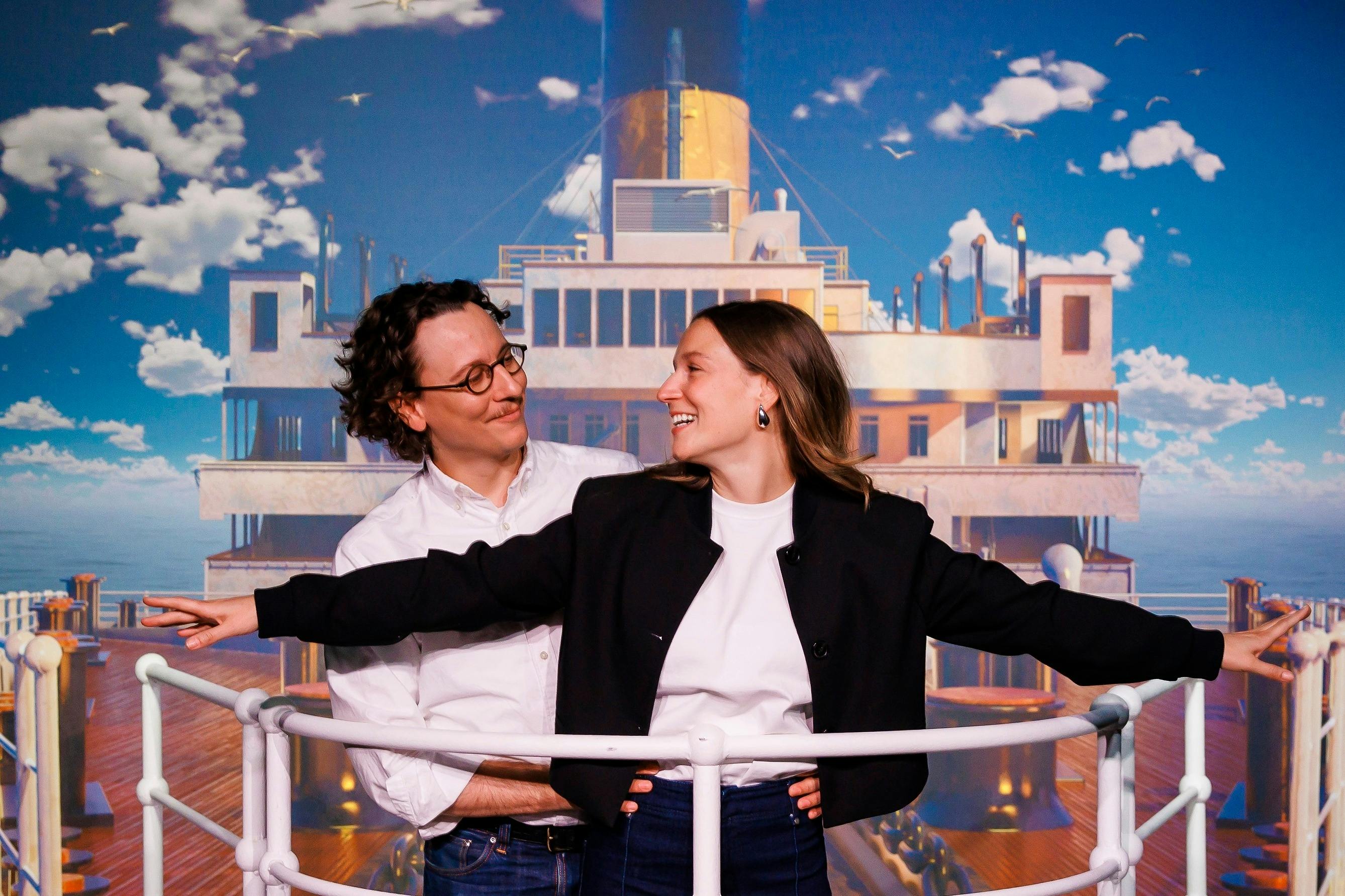 一男一女在建筑和多云的天空的背景下微笑着在船的甲板上摆姿势。