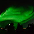Silhouettes de passagers observant une aurore boréale verte sur un bateau.
