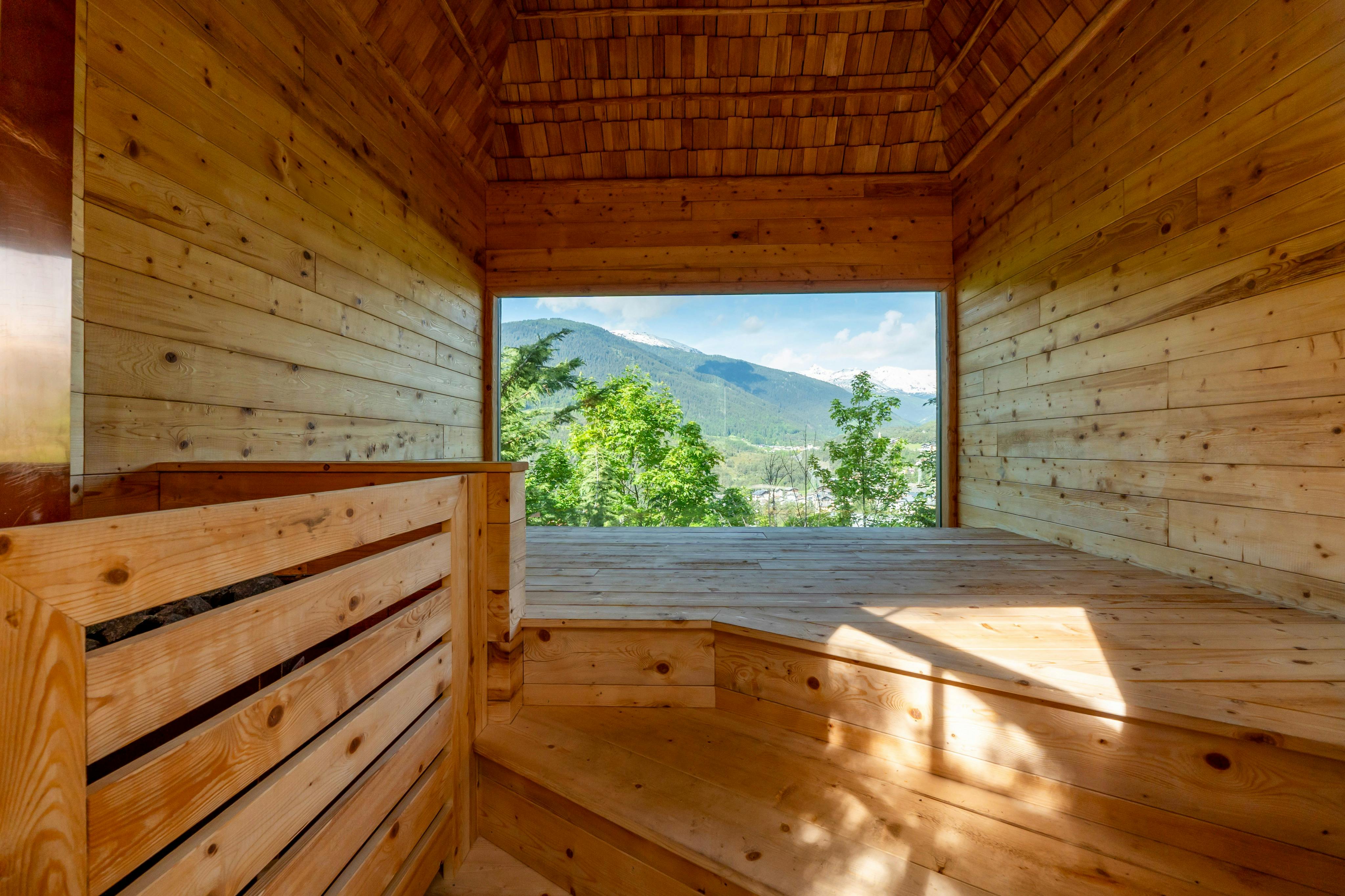 A wooden interior with a large open window framing a scenic view of mountains and trees under a blue sky.