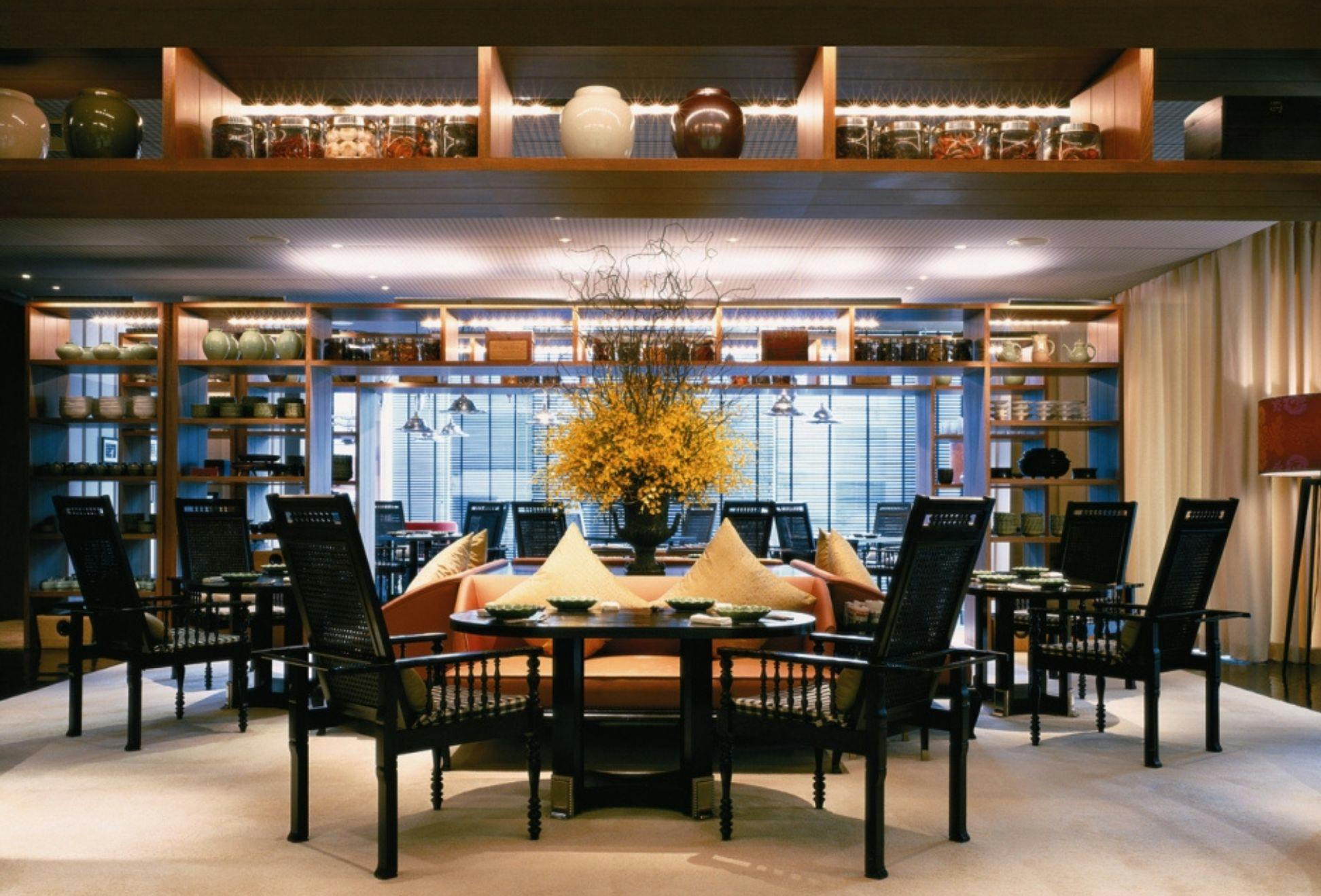 A stylish dining area with wooden furniture, yellow cushions, and a centerpiece of yellow flowers under warm lighting.