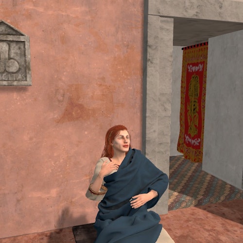 Una persona con lunghi capelli rossi, drappeggiata in un tessuto blu, seduta contro una parete strutturata vicino a una porta con una tenda colorata all'interno.