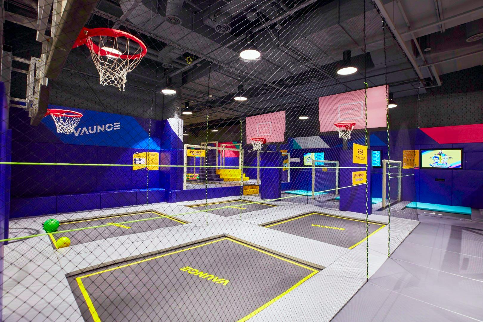 Indendørs trampolinpark med basketballbøjler, levende vægge og sikkerhedsnet. "Vaunce" mærke synligt på trampoliner.