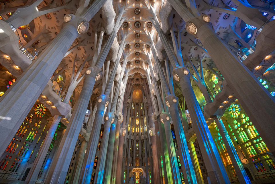 Interior of Sagrada Família, featuring tall, ornate columns, intricate ceilings, and colorful stained glass windows.