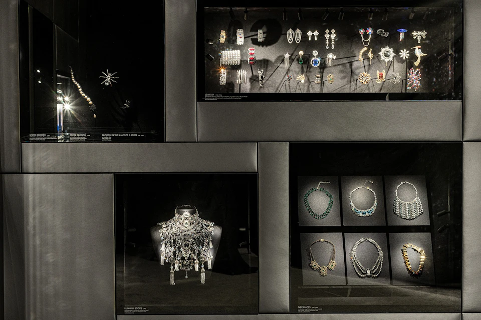 Glass display cases showcasing various jewelry, including brooches, earrings, bracelets, and necklaces, set against a dark background.