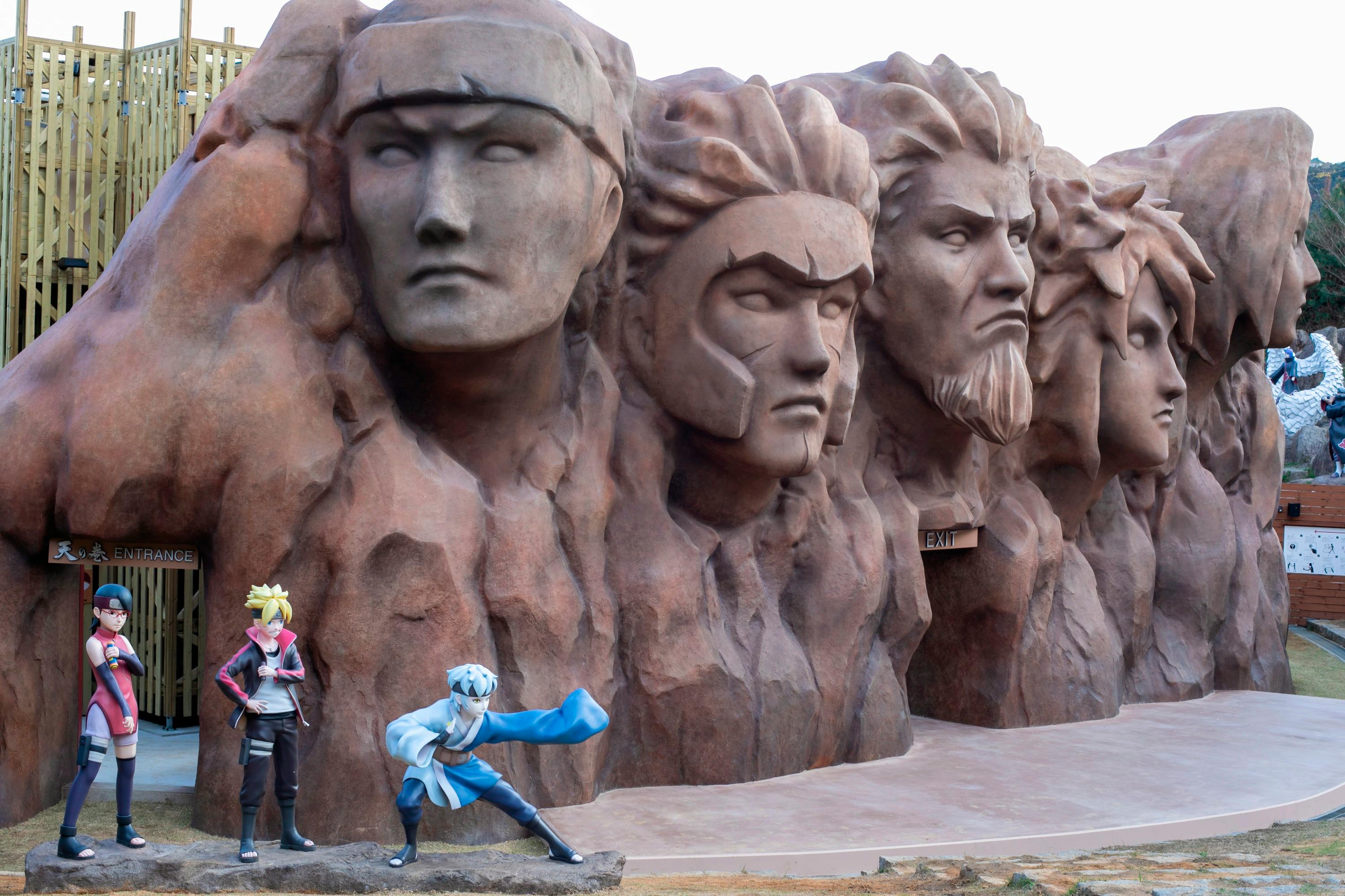 A sculpture depicting five large carved faces on a rock wall, with a character in blue posing dynamically in the foreground.