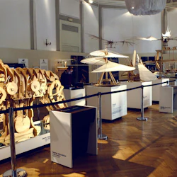 Utställningsrum med mekaniska trämodeller, inklusive ett lejon och flygande maskiner. En person observerar displayerna.