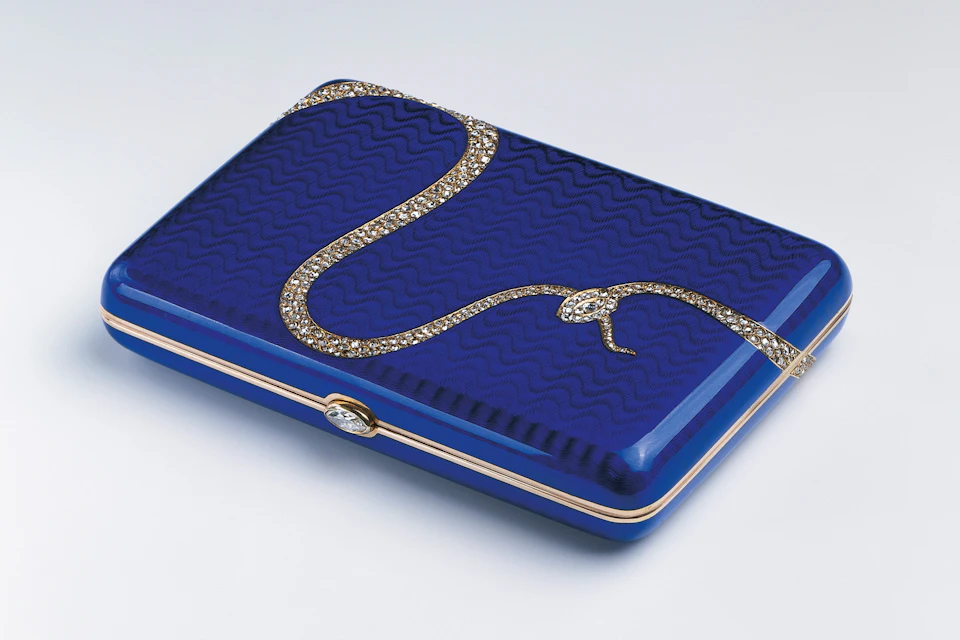 A rectangular blue clutch with a gold snake-shaped embellishment on its surface against a white background.