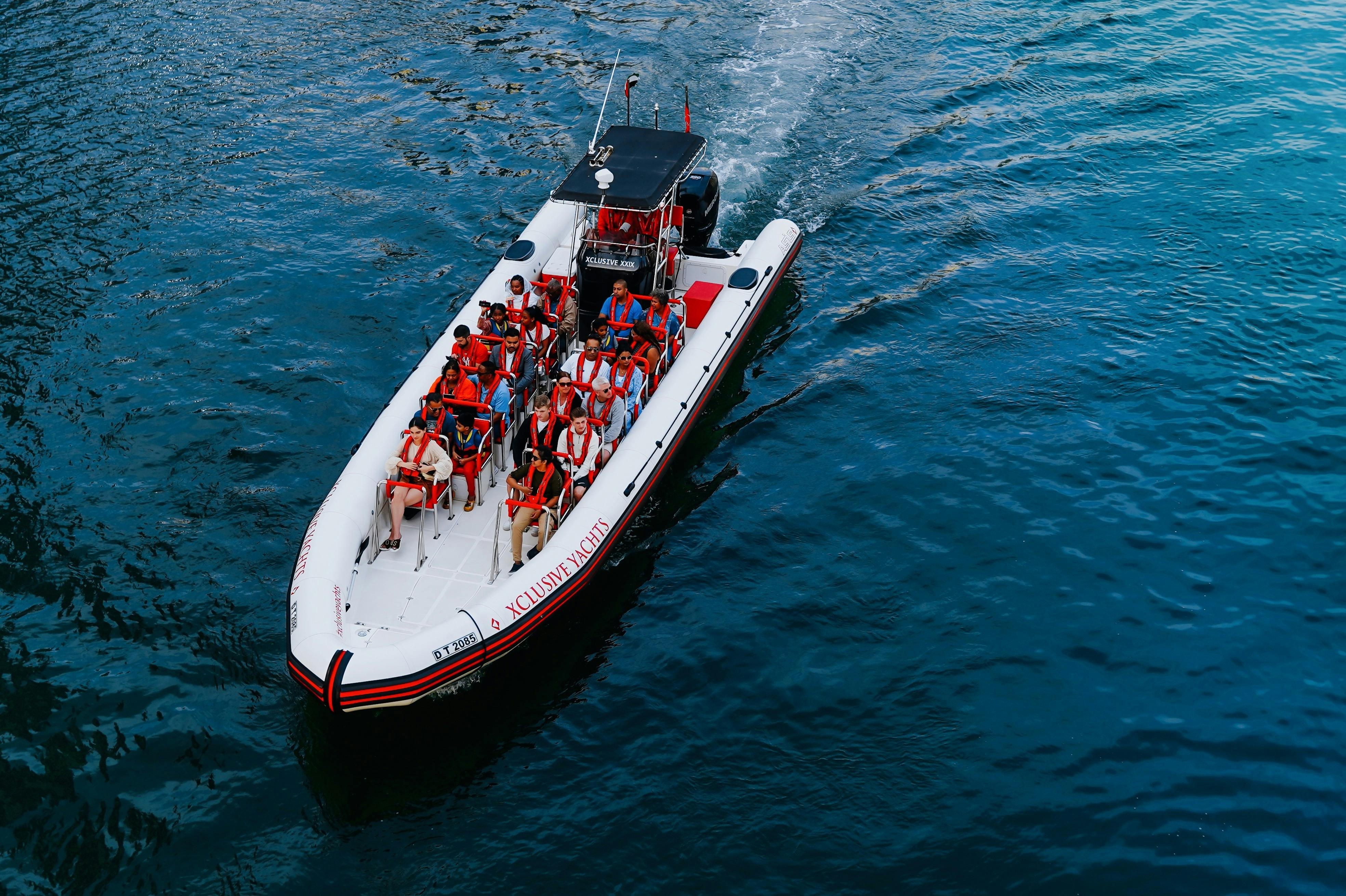 オレンジ色のライフジャケットを着た数人のボートが青い水の中を移動しています。