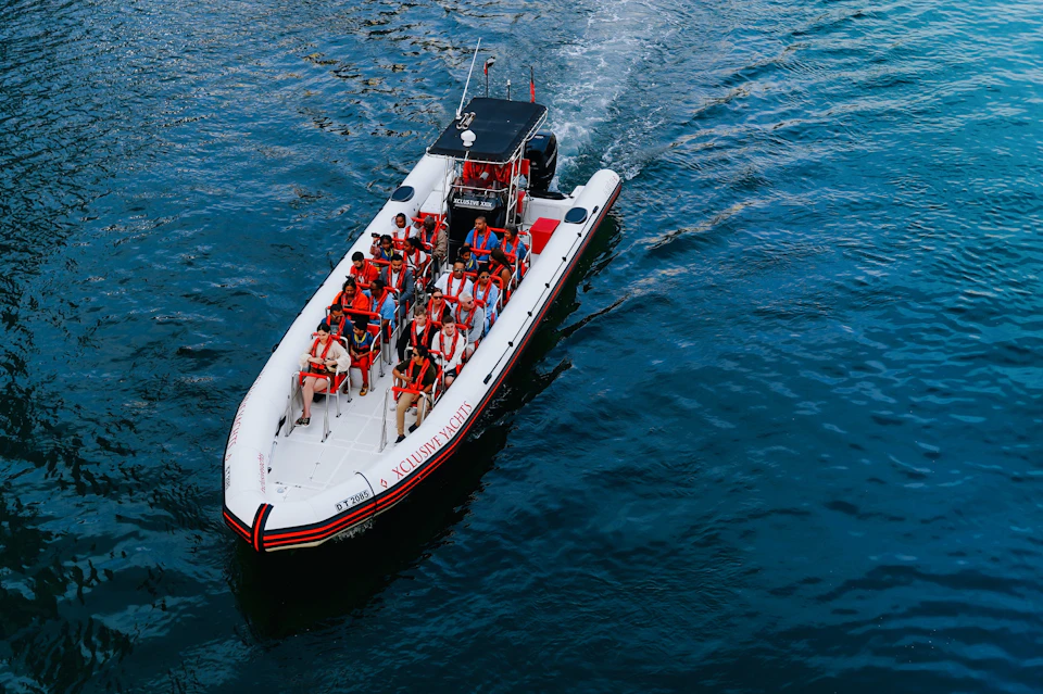 A boat with several people wearing orange life jackets is moving through blue water.