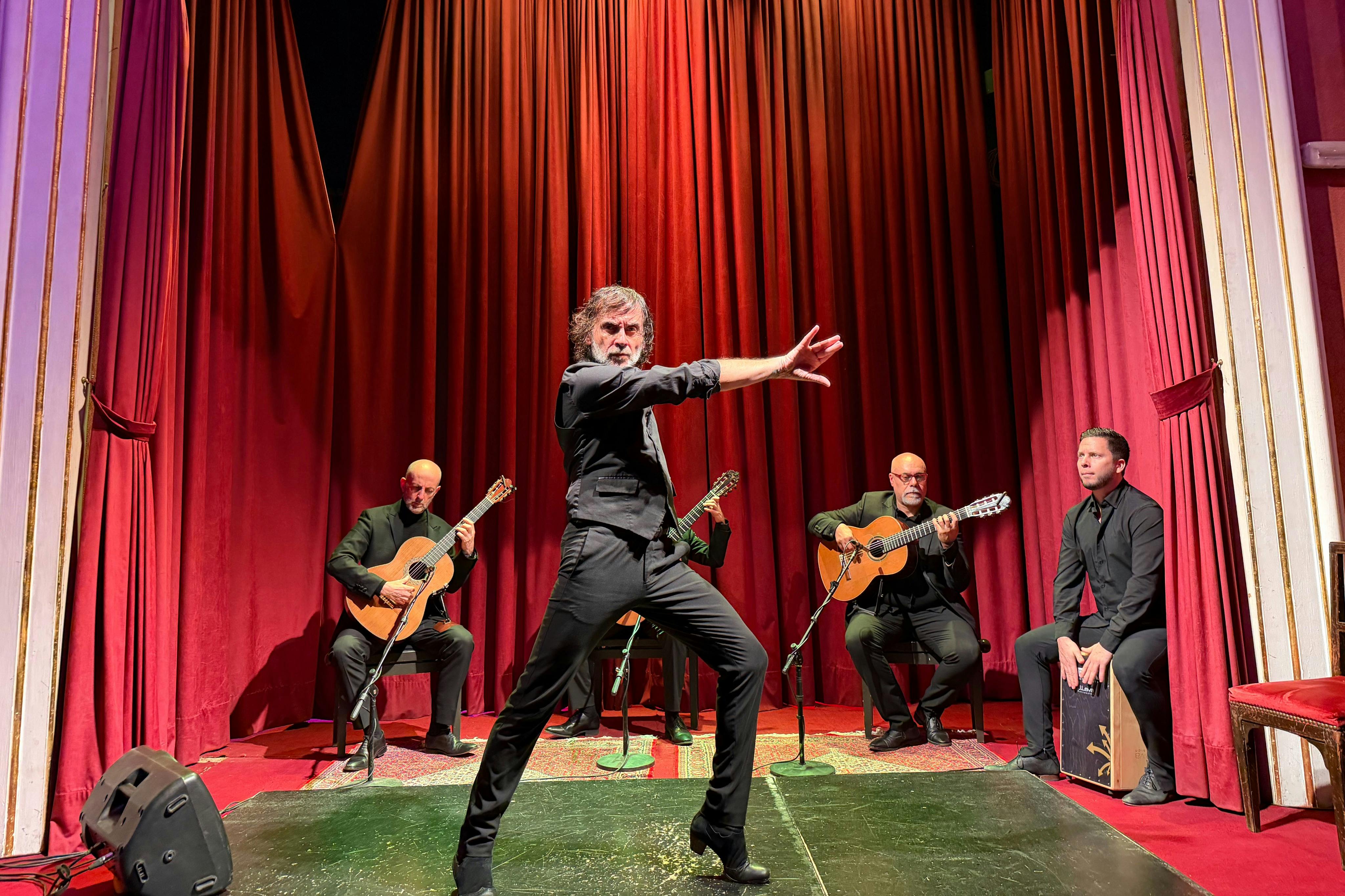 Une danseuse de flamenco se produit devant trois guitaristes et un percussionniste sur une scène aux rideaux rouges.