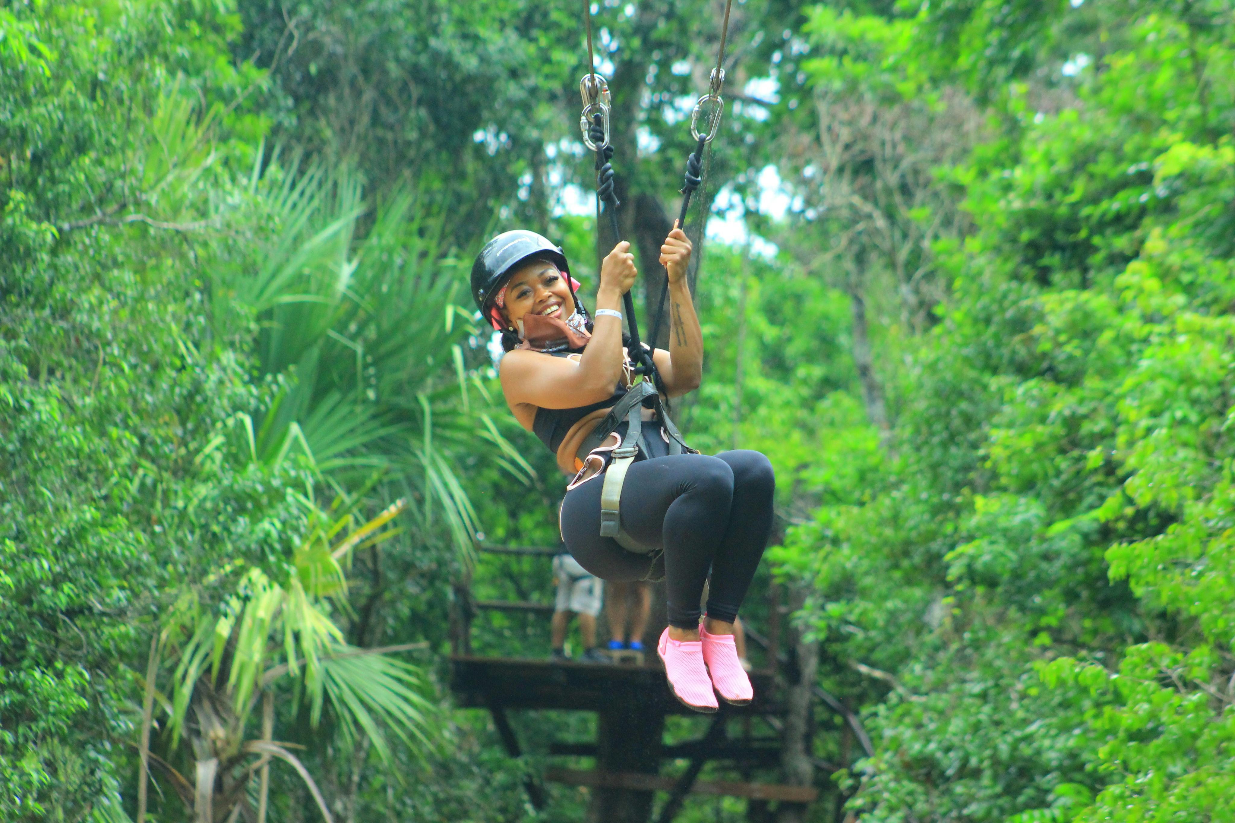 Une personne en tenue de sport, souriante, fait de la tyrolienne dans une forêt verdoyante.