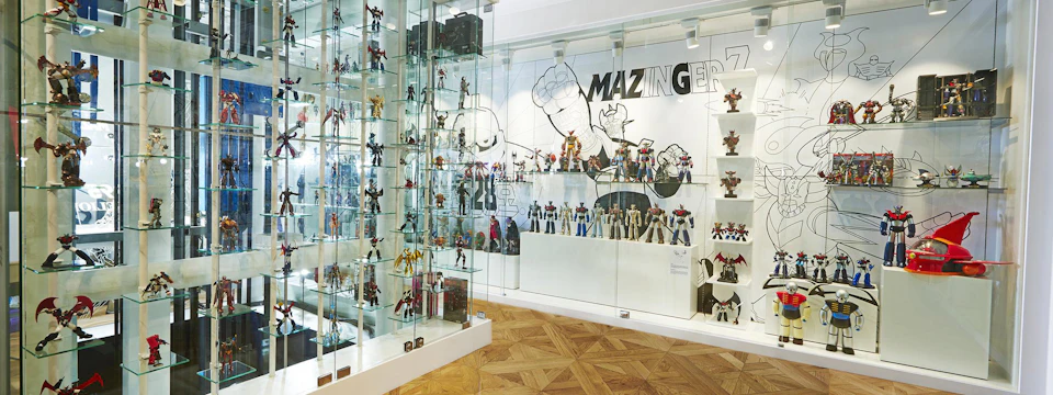 A display room with shelves full of robot figures and a wall mural featuring the text 'Mazinger' and character artwork.
