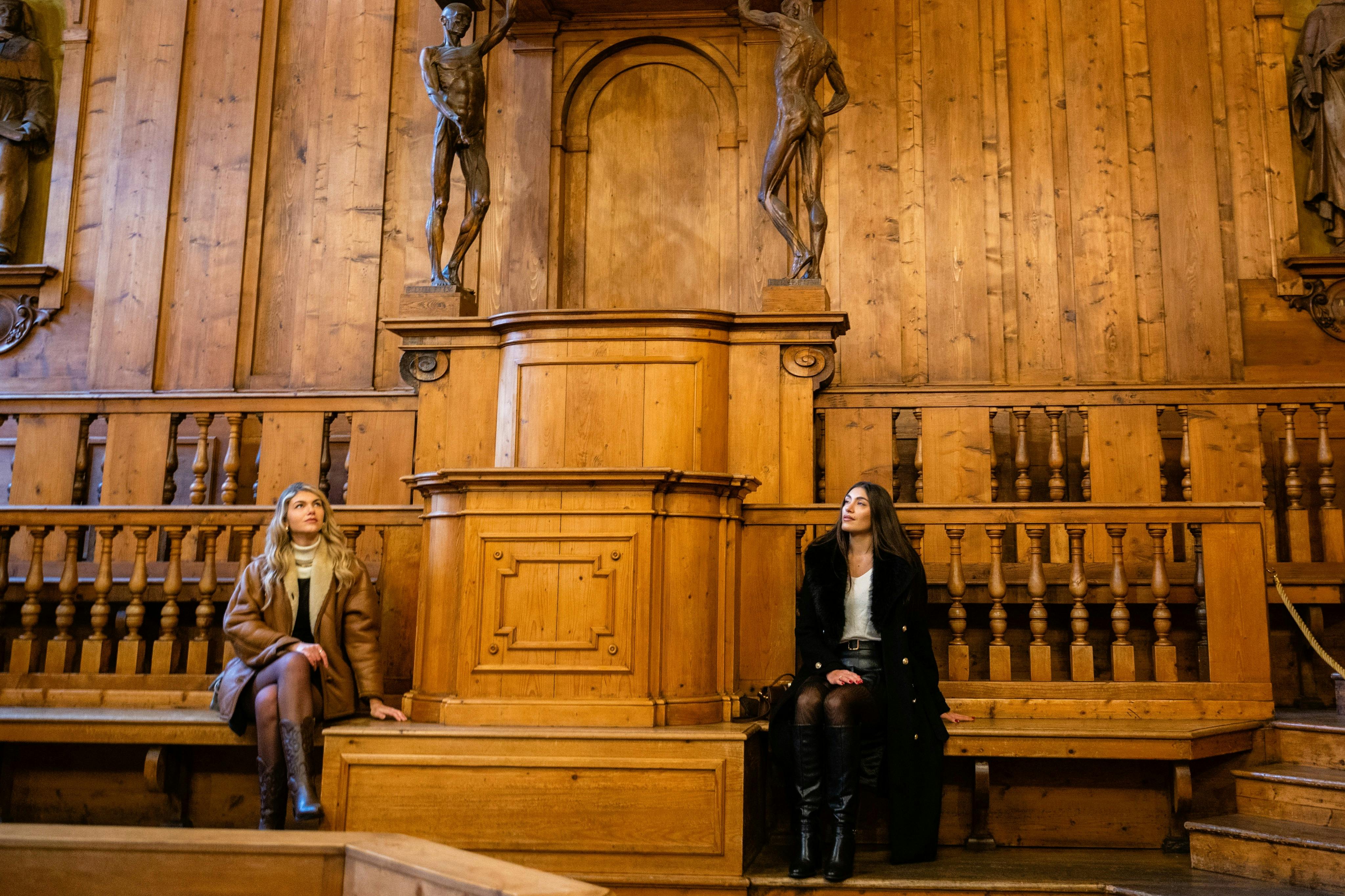 Due donne sedute in una storica sala di legno con intagli e statue ornate, una su ciascun lato di un podio centrale di legno.