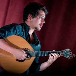 Person som spelar ett stränginstrument mot en mörkröd gardinbakgrund.