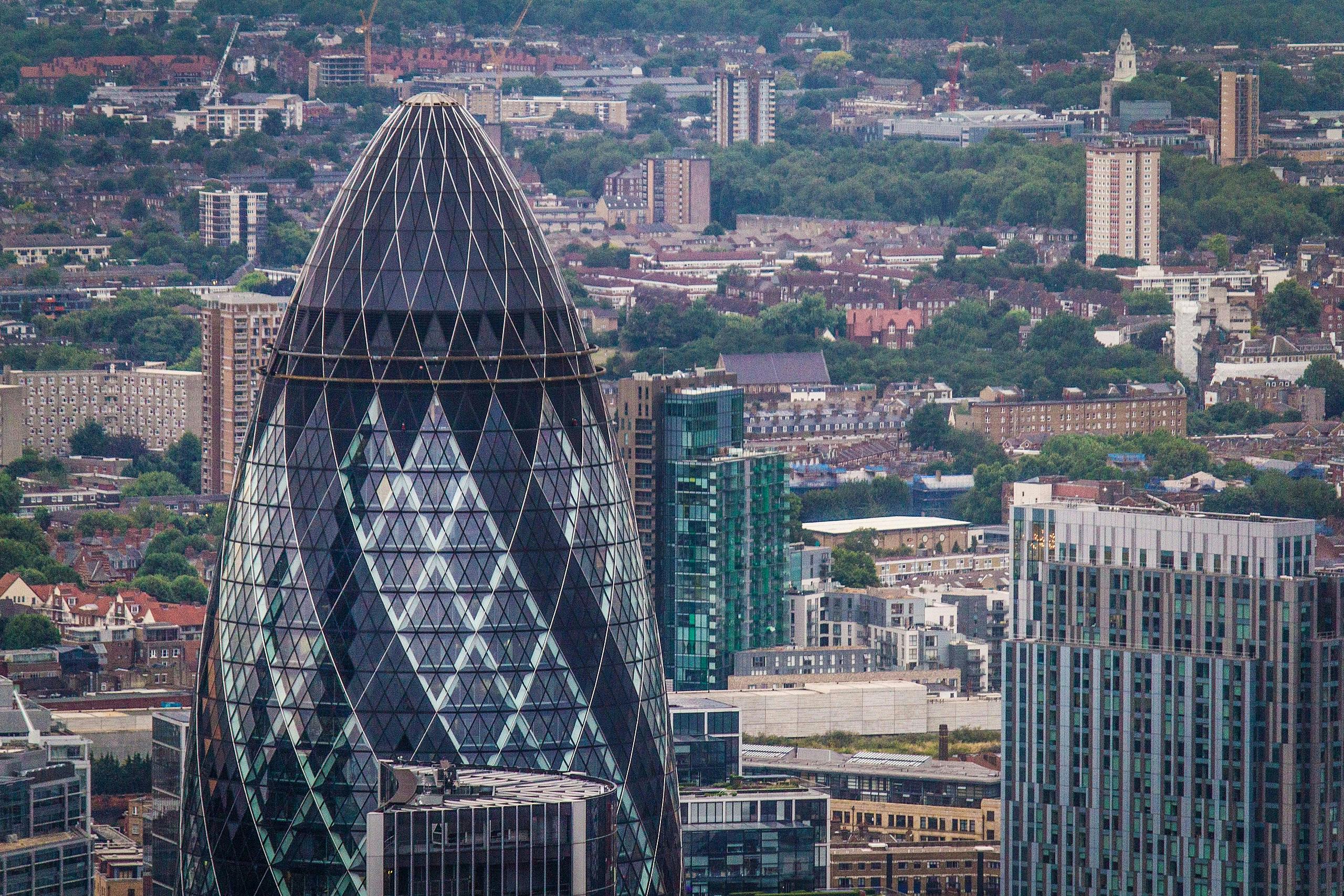 Grande plano do edifício Gherkin, coberto de vidro, com um pano de fundo de edifícios urbanos e vegetação.