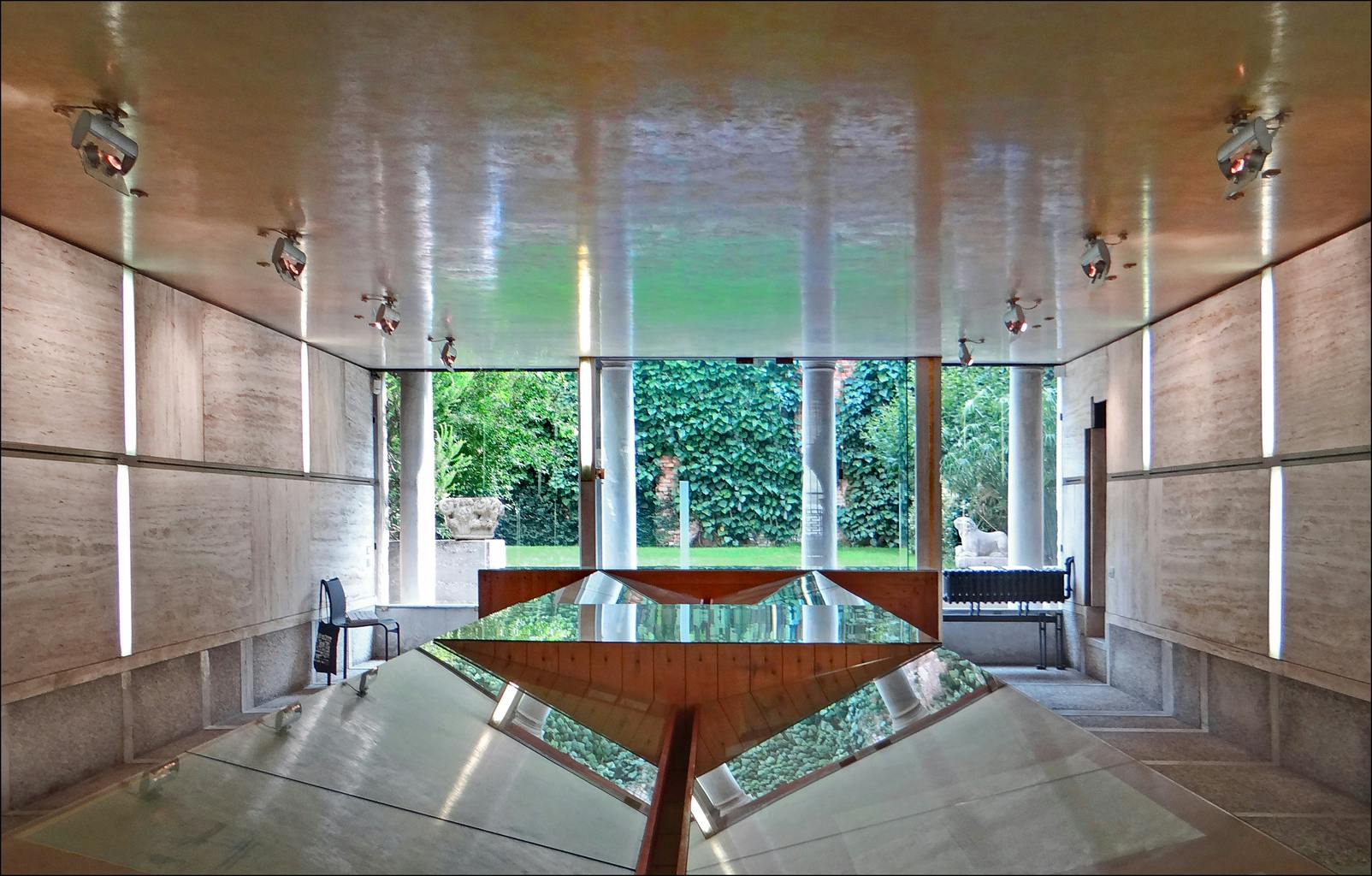 一间现代化的房间，有反光表面和一扇通往郁郁葱葱的花园的大窗户，花园里有树木和雕像。