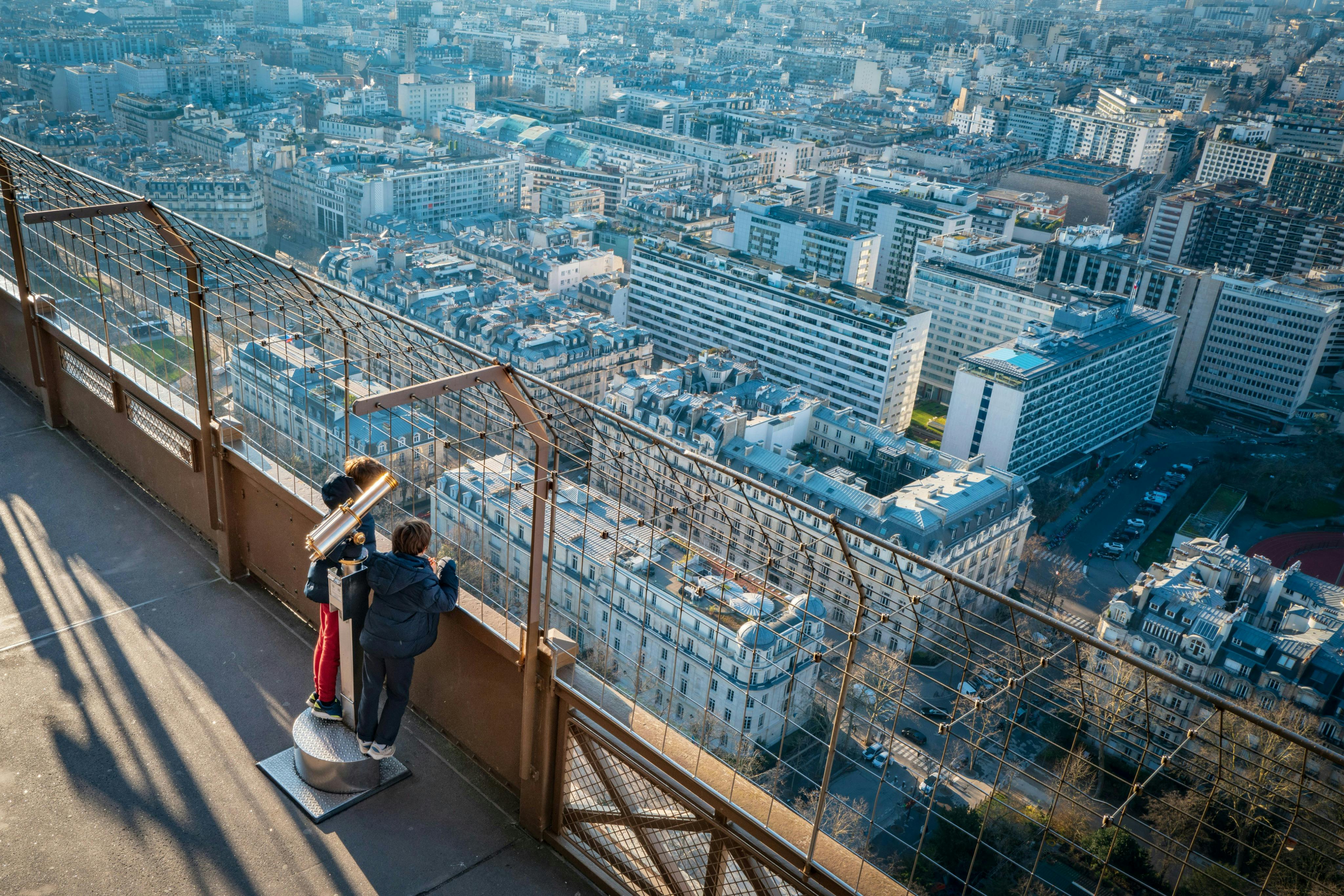 两个人站在一个带取景器的观景台上，俯瞰着有建筑物和街道的城市景观。