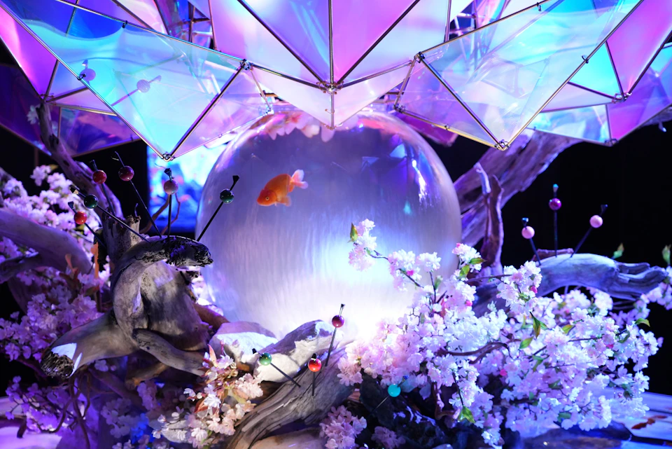 A decorative scene with a glowing orb containing a goldfish, surrounded by cherry blossoms and illuminated geometric shapes.
