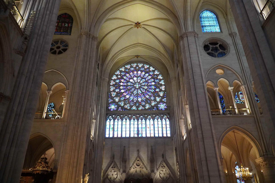 Interior view of a cathedral showcasing a large, intricate stained glass rose window and high vaulted ceilings.