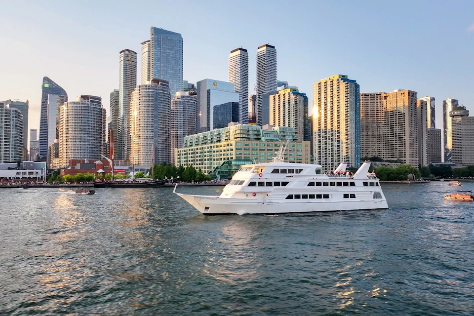 A white boat cruising on a river with a cityscape of tall buildings in the background under a clear sky.