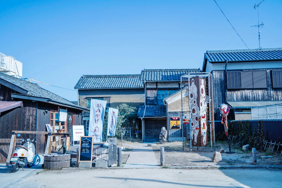 A traditional Japanese building with decorative banners, signs, and small sculptures under a clear blue sky.