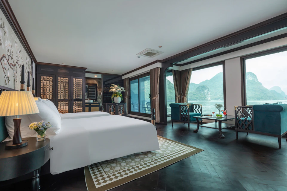 Spacious bedroom with a large bed, armchairs, and a coffee table, featuring a view of mountains through glass doors.