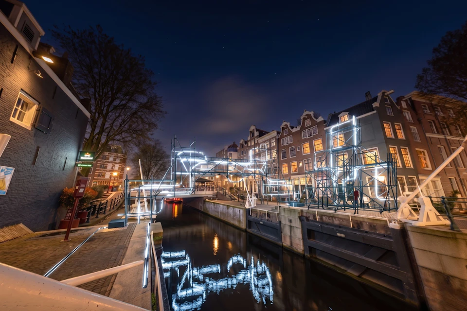 Illuminated canal bridge and buildings at night with reflective water and a clear sky.