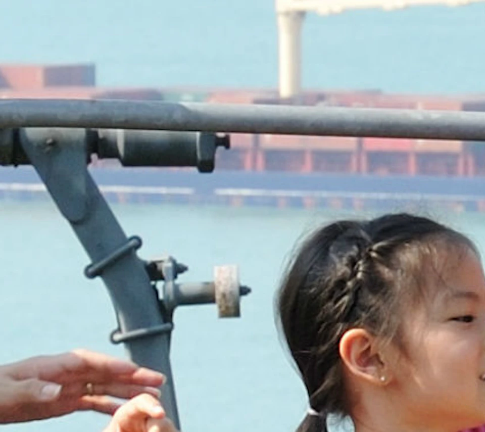 Family of four sitting on a chairlift, enjoying a scenic view of the sea with ships and a distant shoreline.