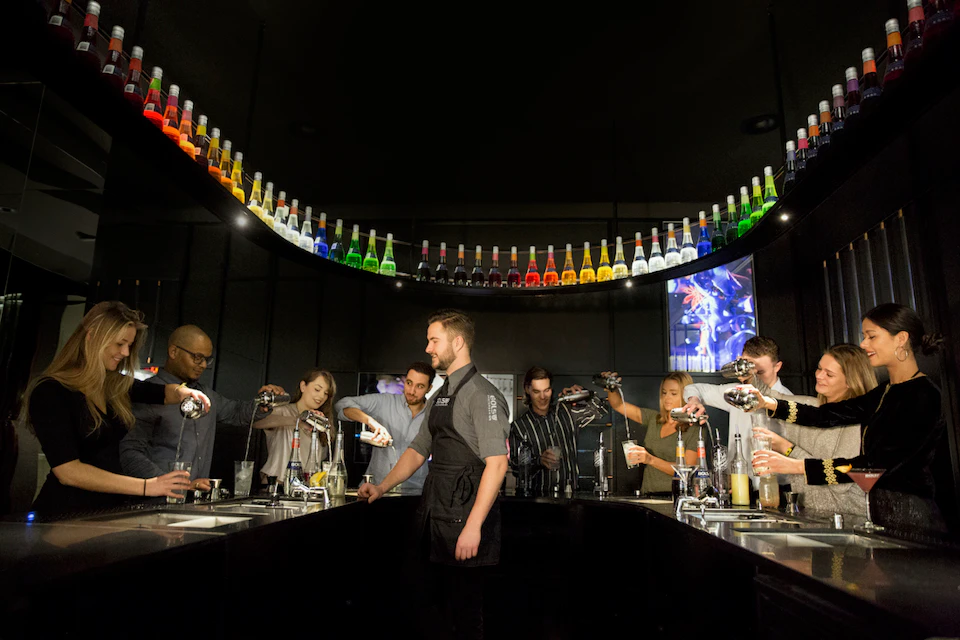 A bartender assists a group of people mixing drinks under a colorful display of bottles in a modern bar setting.