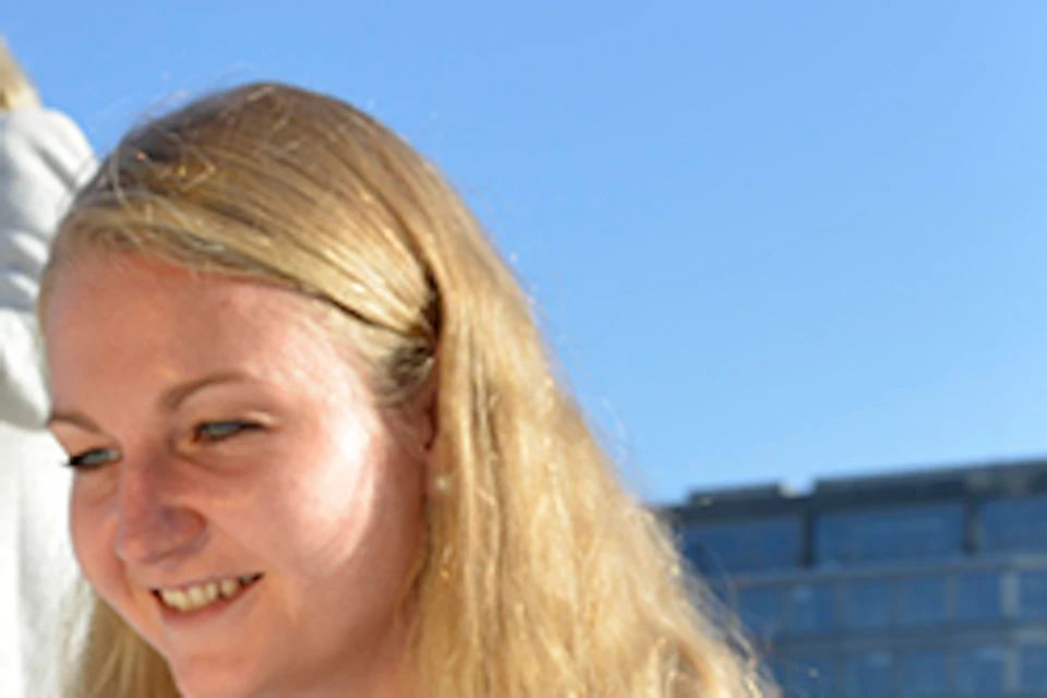 A woman sitting outdoors, smiling while reading a folded map, with two other women and modern buildings in the background.