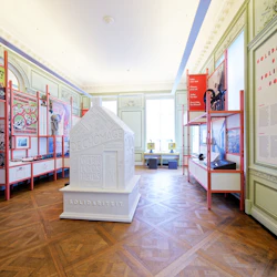 En museiutställning med informationsaffischer, foton och en central vit skulptur i ett dekorativt rum med trägolv.