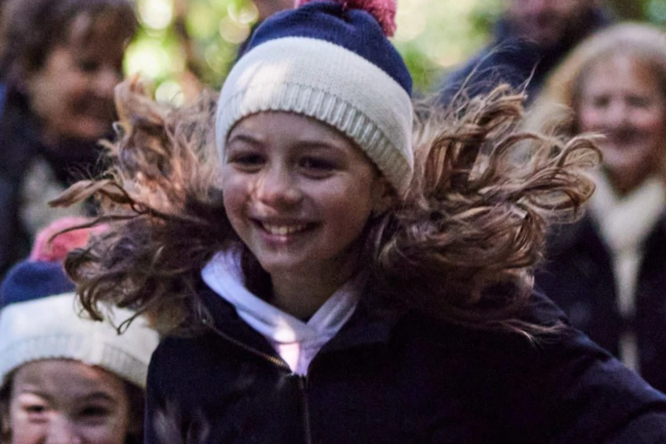Children running on a wooden walkway through a forest, followed by a group of adults.