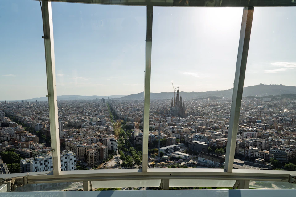 View of a cityscape through large glass windows, with a prominent cathedral and hills in the distance under a clear sky.
