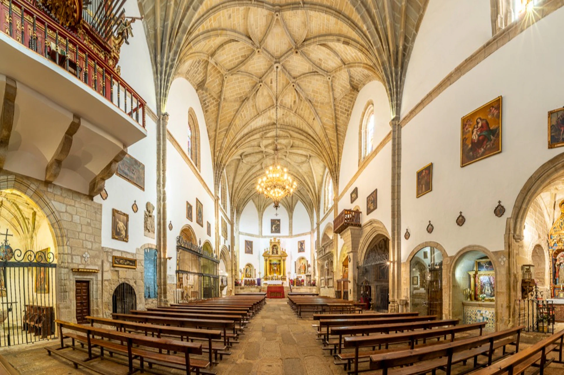 Interior of a historic church with vaulted ceiling, wooden pews, ornate chandelier, and altar in the background.