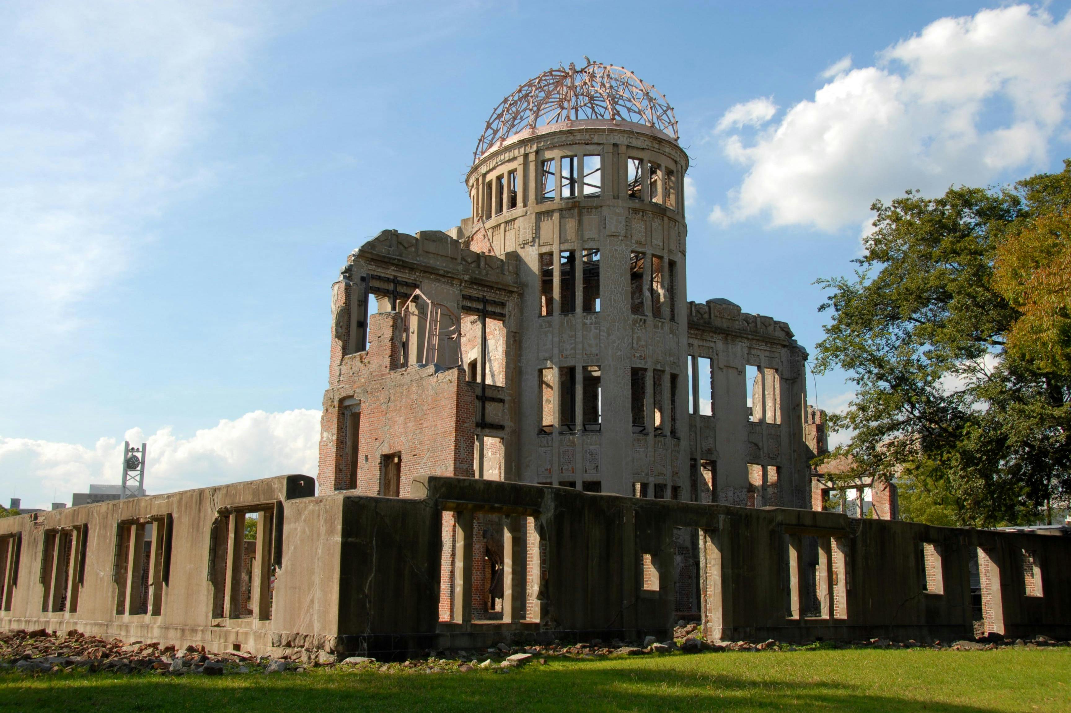 A partially destroyed building with a dome structure, set against a blue sky with clouds and surrounded by a grassy area.