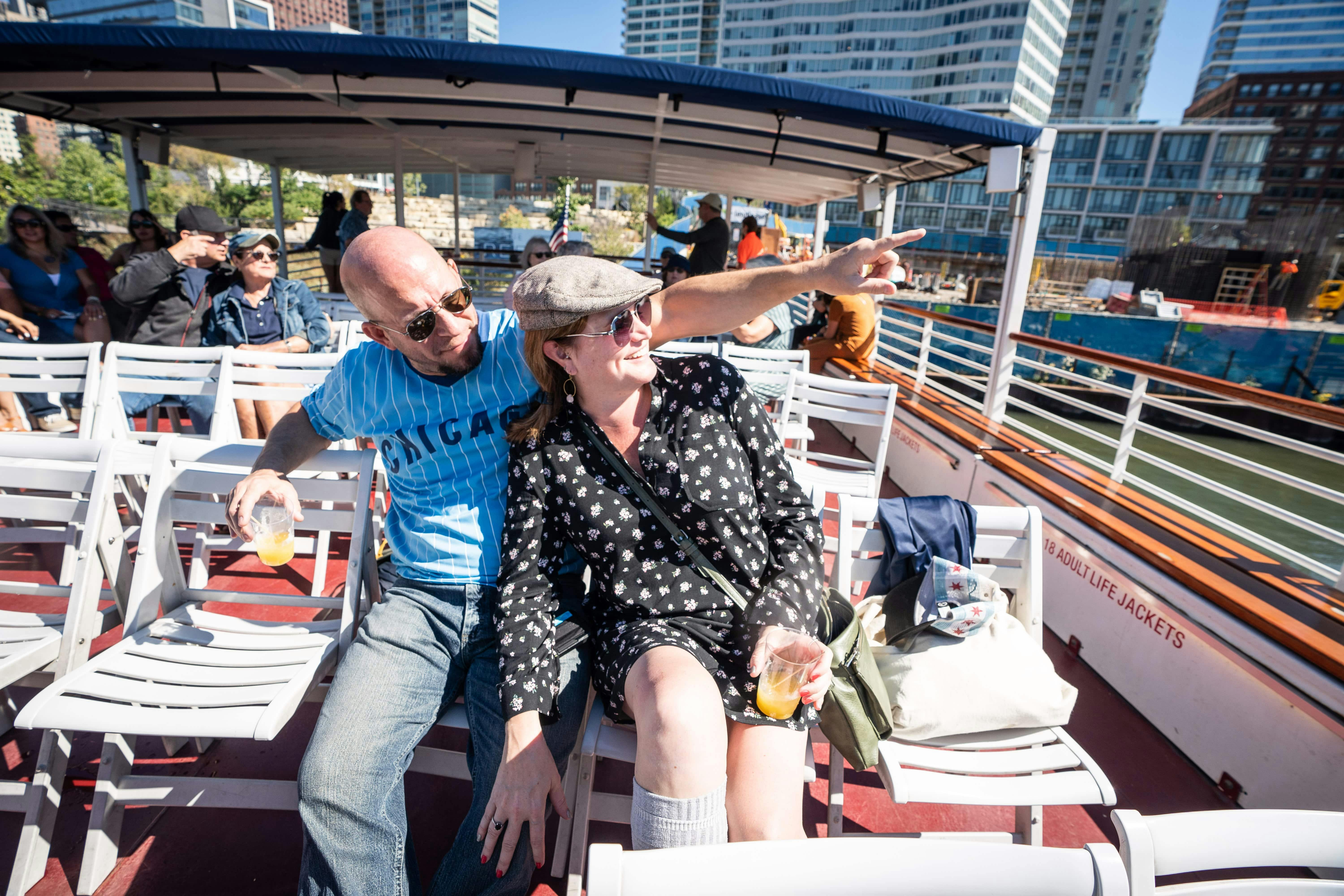 白い座席のボートに座っている男性と女性。男性は飲み物を持っている間に指さし、女性は笑顔で飲み物を持っています。